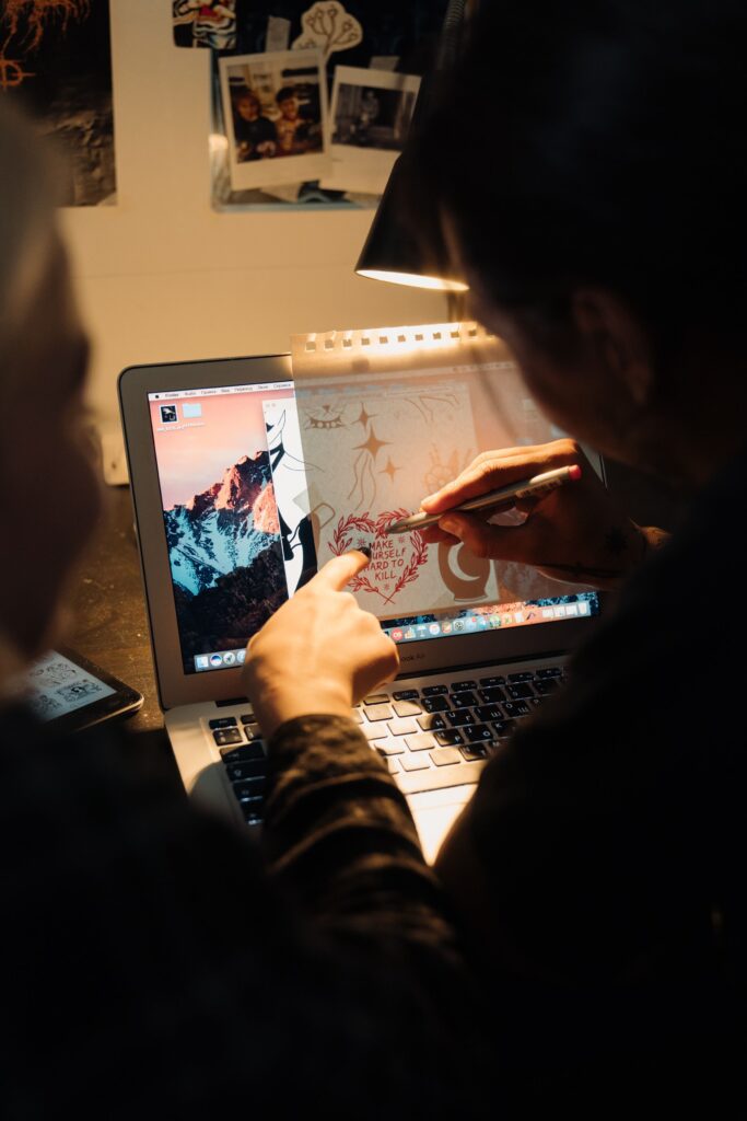 An artist sketches a design on a laptop, blending digital and traditional art techniques.